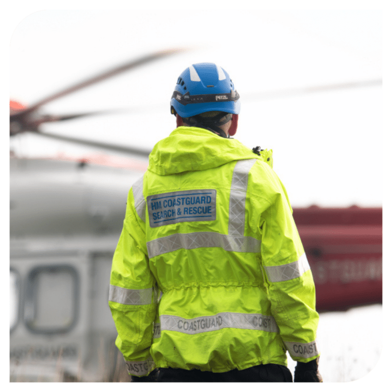 Back of HM Coastguard Search and Rescue worker stood in front of a helicopter