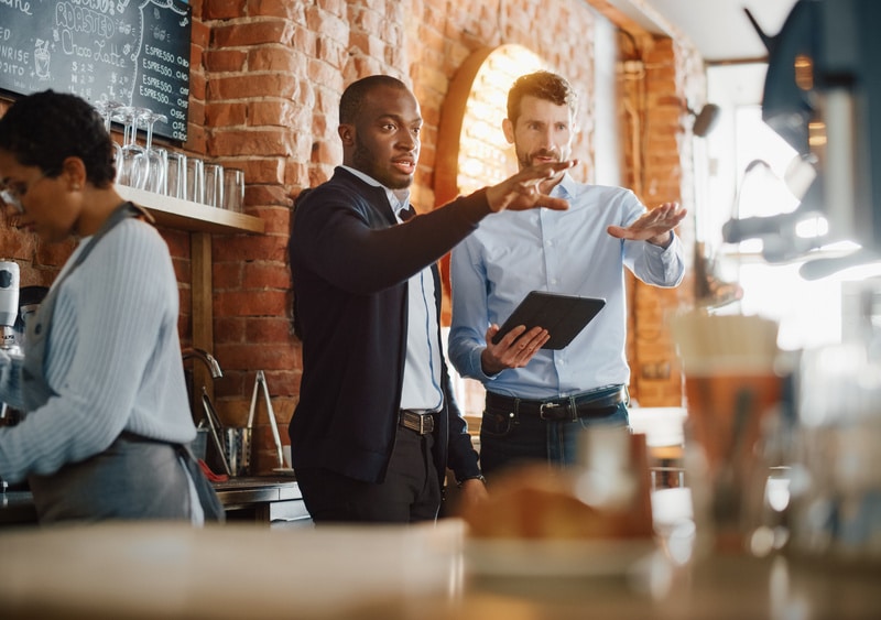Meeting Behind the Counter and Working on Tablet Computer and Checking Inventory in a Cozy Loft-Style Cafe. Successful Restaurant Managers and Barista at Work