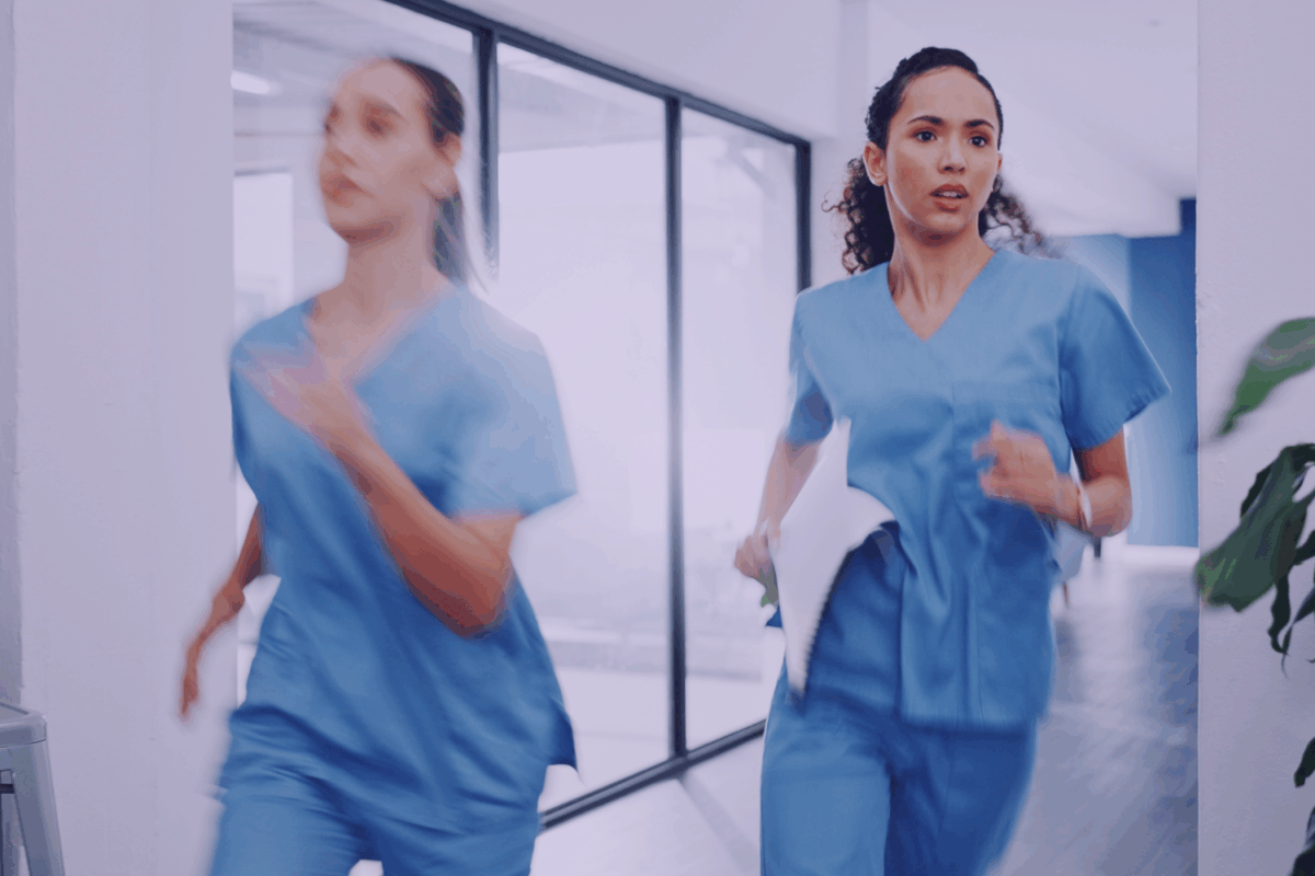 two female healthcare workers running along a hospital corridor, looking determined but concerned