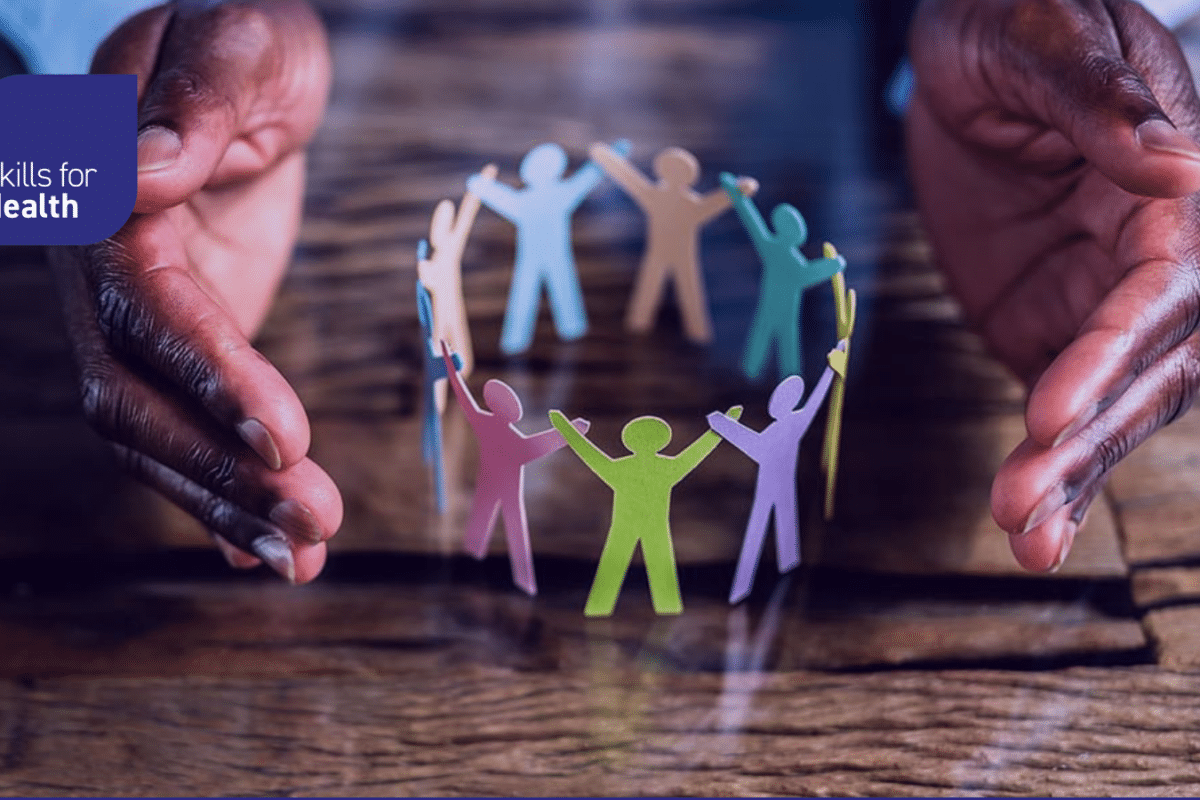 hands hovering over a paper cutout of human silhouettes handing hands in a circle