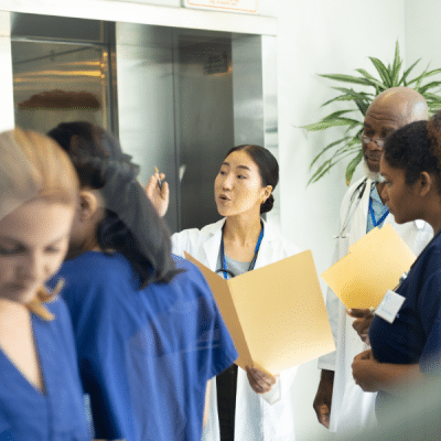 Diverse group of male and female doctors holding files discussing in busy hospital corridor.