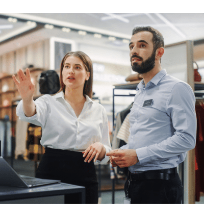 business woman uses laptop computer and speaks to colleague in shop environment