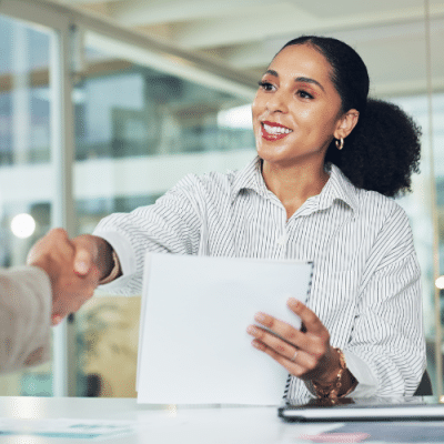 Woman in an office environment holding a document and shaking hands with someone.