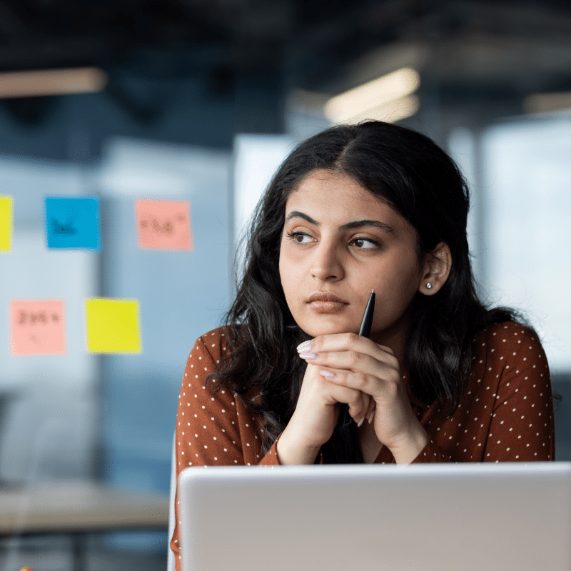 Person looking reflective in an office at a laptop