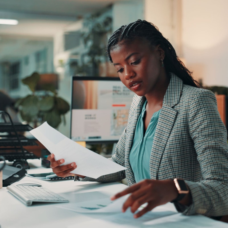 Person working at a desk in an office, they are reviewing paper documents.